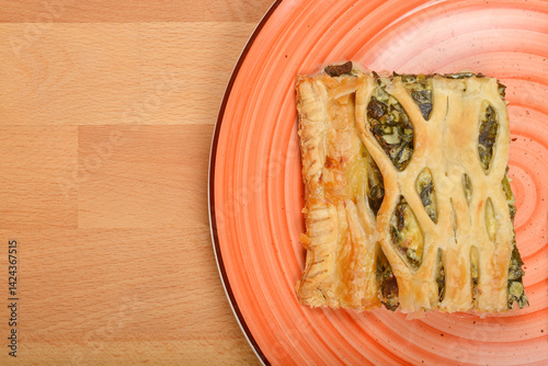 A slice of baked savory pastry with a lattice top and spinach filling sits on a colorful plate against a wooden surface