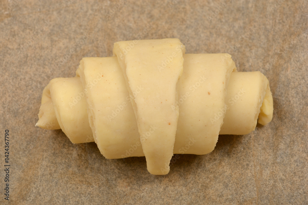 A single, unbaked croissant dough rests on a piece of parchment paper, ready for the oven