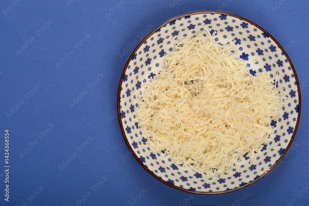 A patterned bowl contains a pile of freshly grated horseradish on a solid blue surface
