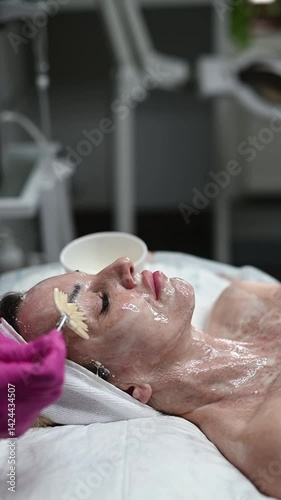 Facial cleansing, foamy essence, vertical, brush application, general. A skincare specialist gently applies a rich foamy essence to the client’s face using a soft cosmetic brush.