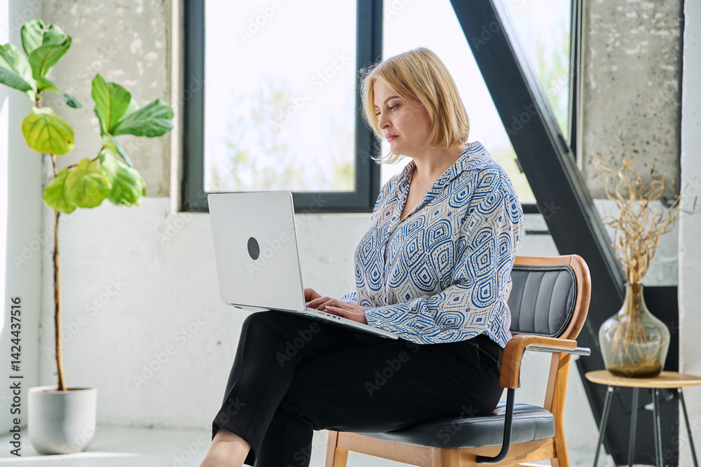 Serious middle aged business woman sitting in chair typing on laptop computer