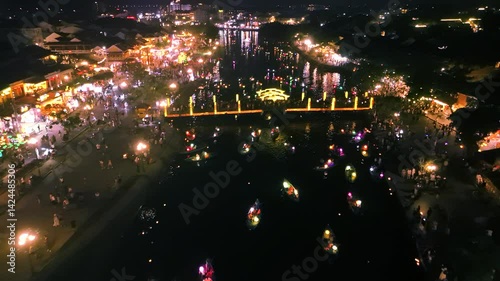 Nighttime aerial panorama showing illuminated bridge, thu bon river, colorful boats amid festive crowds during hoi an's vibrant full moon celebration in vietnam