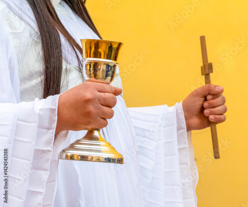 Angel dressed in white, holding a golden chalice and a wooden cross, takes part in a Good Friday procession.