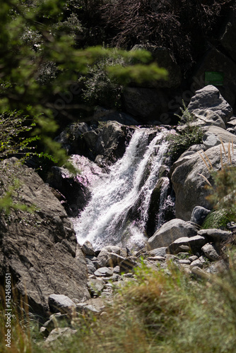 Shaded waterfall surrounded by vegetation and large boulders. Captured in soft light, emphasizing the contrast between rock textures and flowing water. A tranquil nature detail for wellness and travel
