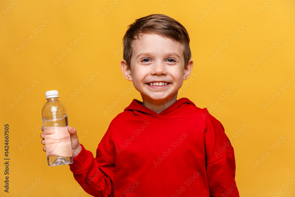 A happy little boy drinks water for health on yellow background. The child is holding a water bottle. A kid with a plastic bottle. Children's activity and energy, generation Z. body hydration concept