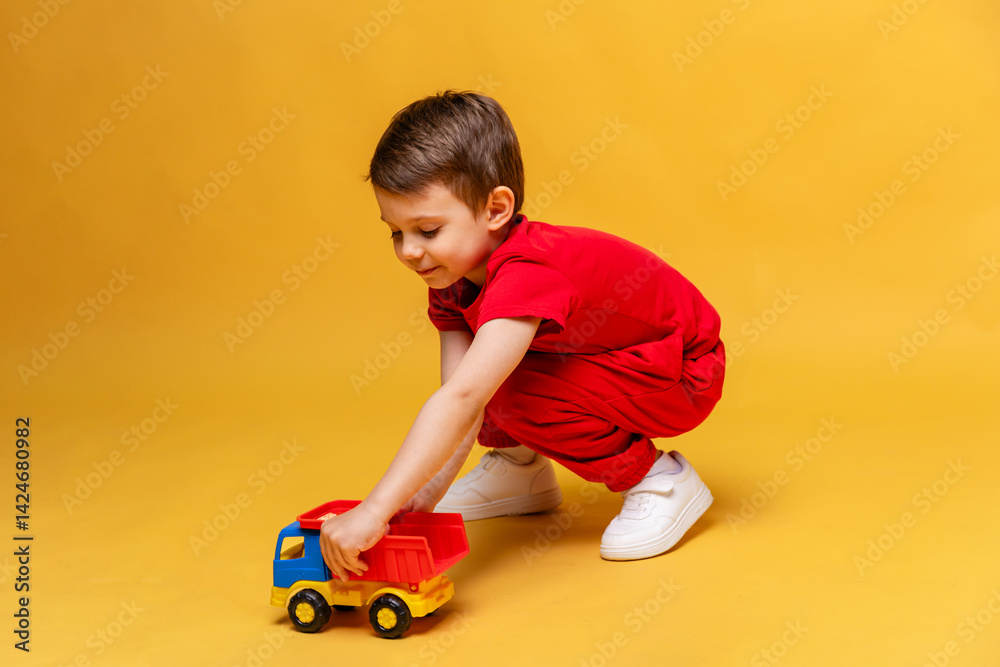 Child, little boy in red sport suit playing with toy car on yellow background. Childhood education, kindergarten and development concept, Space for text. High quality photo.