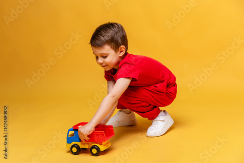Obraz na płótnie Child, little boy in red sport suit playing with toy car on yellow background. Childhood education, kindergarten and development concept, Space for text. High quality photo. w salonie