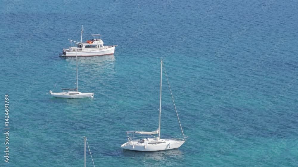Several sailboats anchored in calm blue sea with mountains and coastal town in background. Sunny summer day in Mallorca, peaceful maritime scene, themes of travel, vacation, sailing, and nature. Several sailboats anchored in calm blue sea with mountains and coastal town in background. Sunny summer day in Mallorca, peaceful maritime scene, themes of travel, vacation, sailing, and nature.