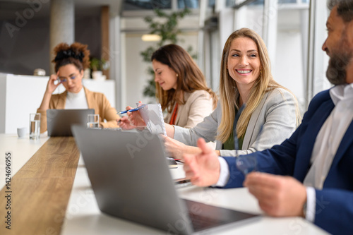 Professional colleagues smiling and discussing project details while working together in meeting room