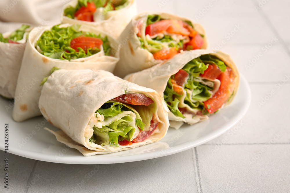 Plate of tasty lavash rolls with tomatoes and greens on white tile background