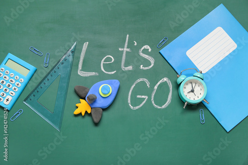 Rocket made of plasticine with different stationery and text LET'S GO on green chalkboard