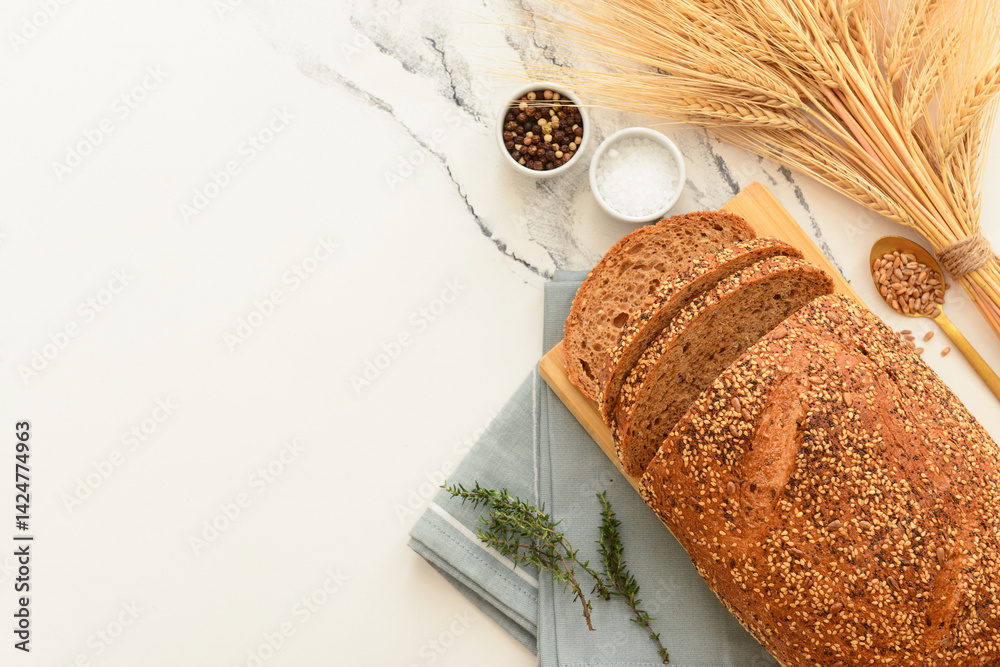Wooden board with sliced loaf of bread, wheat spikelets, grains and thyme on white grunge background
