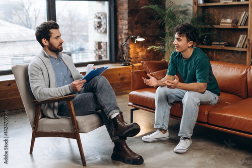 Bild auf Leinwand Smiling teenage boy talking with male psychoanalyst during therapy session