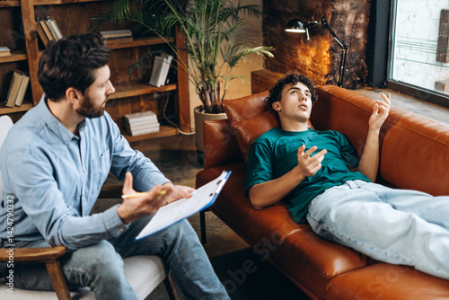 Teenage boy gesturing with hands while talking to male psychologist