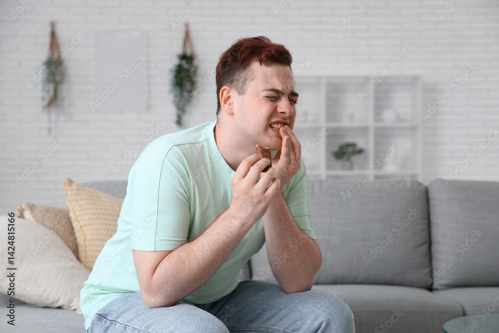 Young man with chocolate suffering from toothache in room Young man with chocolate suffering from toothache in room