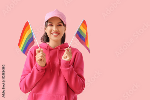 Beautiful young woman with LGBT flags on pink background