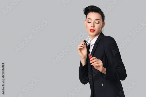 Young pin-up stewardess applying lipstick on grey background