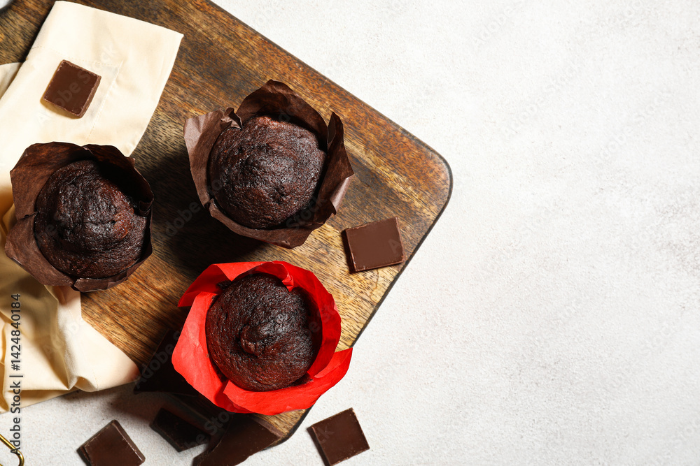 Wooden board with tasty chocolate muffins on white background