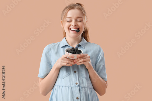 Young pregnant woman eating dried prunes on beige background