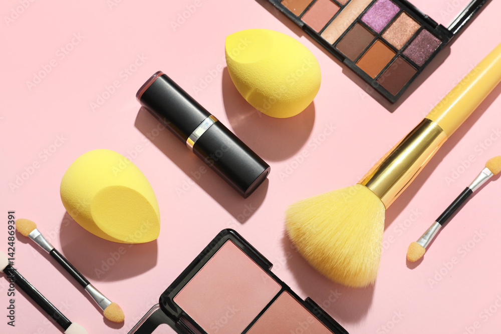 Makeup sponges with yellow brush and different decorative cosmetics on pink background, closeup
