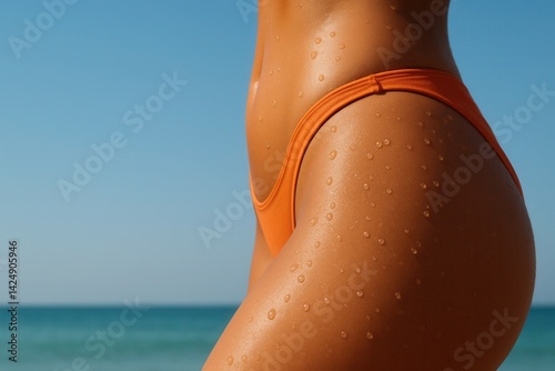 Woman wearing orange bikini bottom showing smooth tanned skin with water droplets at beach