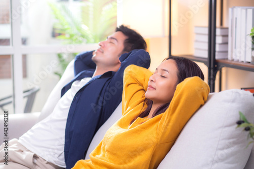 Young asian couple relaxing together on a comfortable sofa at home in the living room, happy and peaceful moment representing love, relationship and modern lifestyle of couple while sitting on couch.
