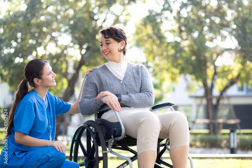 Young caucasian nurse comforting with patient while sitting on wheelchair in outdoor park, doctor woman support and counseling with patient, caregiver and service, medical and consoling.