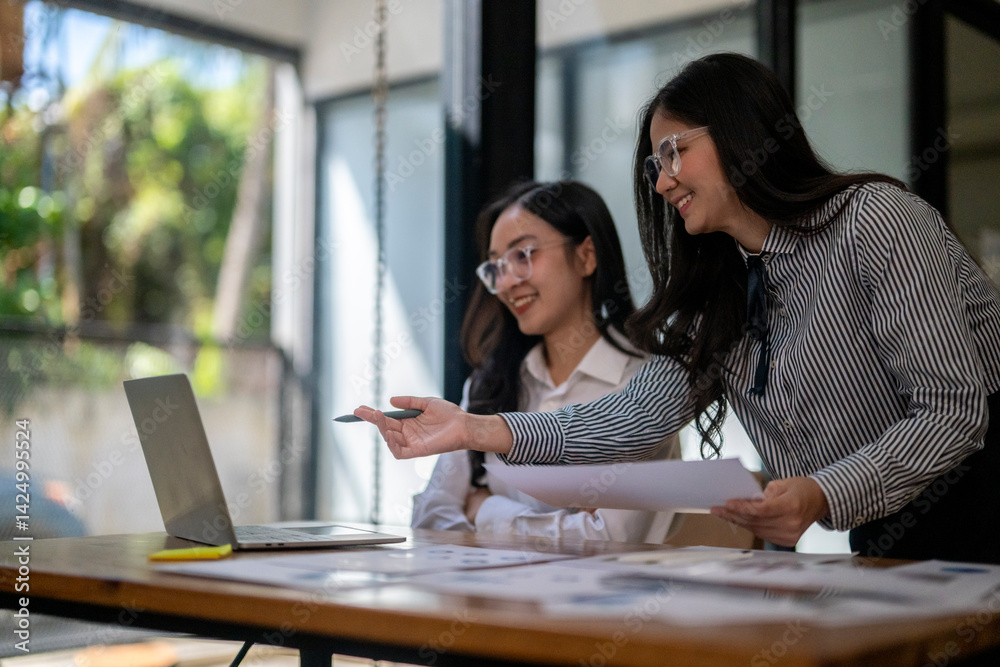 Two women are sitting at a desk with a laptop and a piece of paper Two women are sitting at a desk with a laptop and a piece of paper