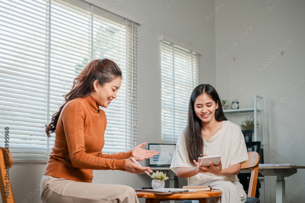 Two women enjoying a casual chat in a home office setting, sharing ideas over a tablet and coffee. Two women enjoying a casual chat in a home office setting, sharing ideas over a tablet and coffee.