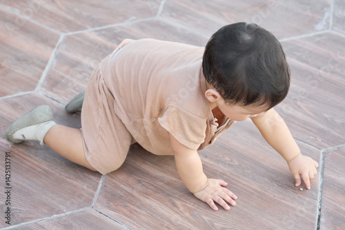 The baby is playing on the floor, reaching out to pick up a small object. The baby's position suggests that they are crawling or in the process of learning how to sit up.