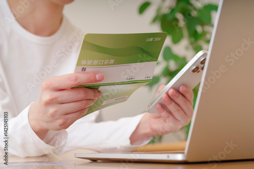 通帳とスマホで金銭のやり取りをする女性