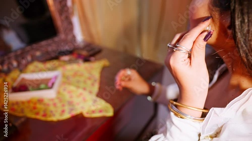 Woman sits calmly fixing sparkly earrings indoors