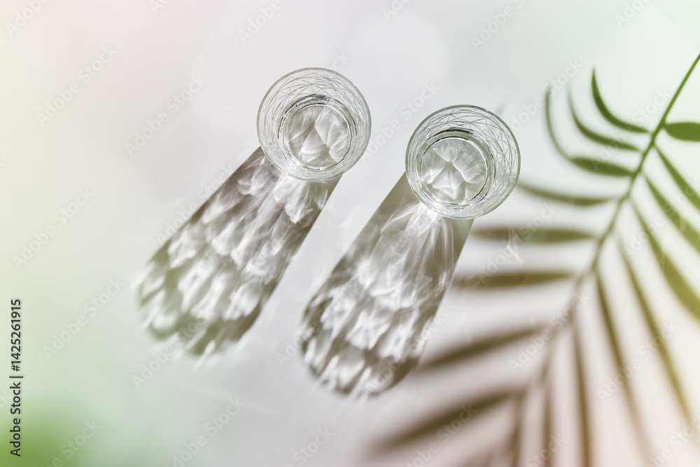 Water Glasses with palm leaf Shadow and sunlight Reflection on white background, colored photo minimal style, aesthetic top view summer still life, refraction throug crystal shine cups, caustic