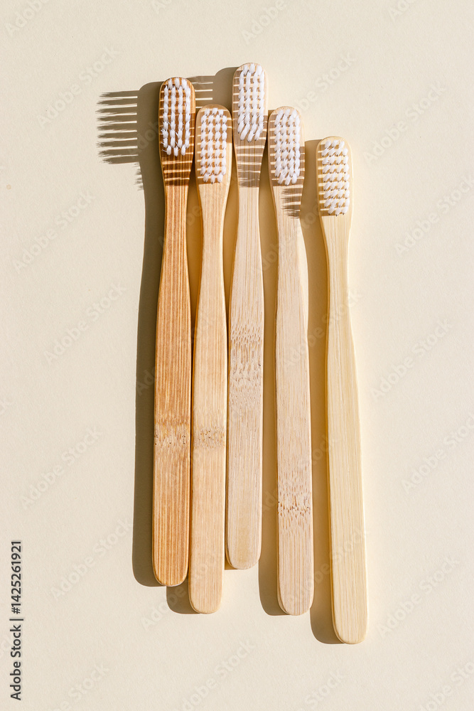 Eco friendly Bamboo toothbrushes with white bristles at sunlight with dark shadows on beige background. Sustainable living concepts, minimal style aesthetic photo, top view set wooden brushes