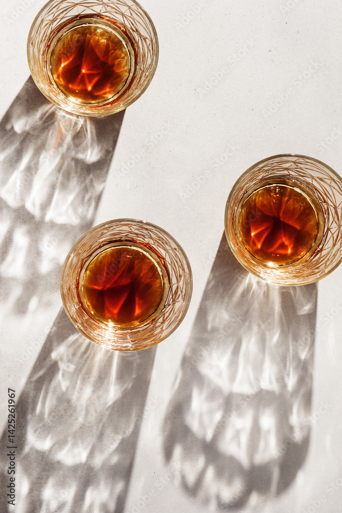 Crystal Whiskey Glasses with shadows at sunlight on beige textured background, minimal aesthetic flat lay shiny glasses, sun glare, stong alcohol drink concept, summer still life top view, copyspace