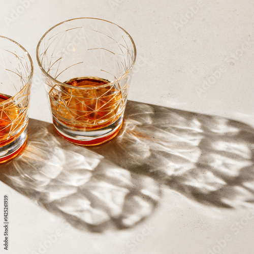 Crystal Glasses with drink, beautiful shadow at sunlight on beige textured background, minimal trend, aesthetic side view shiny glass, sun glare, strong alcohol drink concept, summertime,