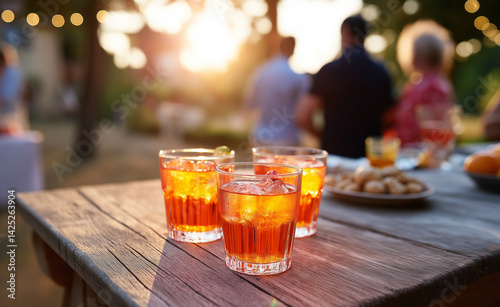 Obraz na płótnie Refreshing orange cocktails on a wooden table at an outdoor gathering during golden hour.
w salonie