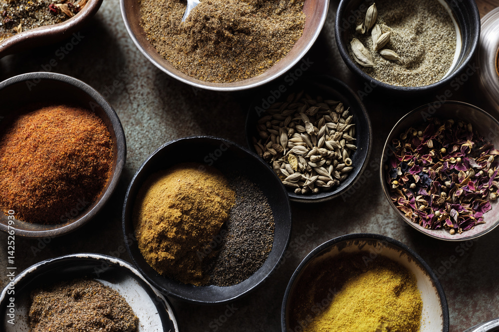 The image shows a variety of spices and herbs in small bowls, including spices like cumin, turmeric, cinnamon, and cardamom, as well as herbs like rose petals and dried lavender