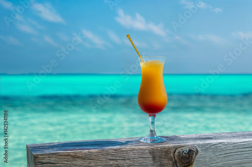 Obraz na płótnie A vibrant orange cocktail with a straw is placed on a wooden railing overlooking a beautiful turquoise ocean under a clear blue sky w salonie