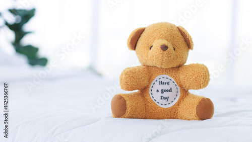 Obraz na płótnie Little teddy bear toy is cute, sitting alone on a comfortable white bed, white pillow and white duvet cover in bedroom at home in morning. w salonie