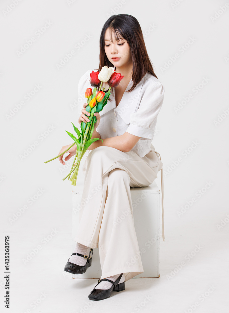 Asian young beautiful pretty happy woman she smiling cute friendly wearing white shirt white pants sitting holding bouquet tulips flowers on white background studio portrait. Lifestyle fashion concept