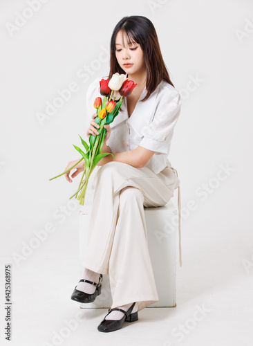 Obraz na płótnie Asian young beautiful pretty happy woman she smiling cute friendly wearing white shirt white pants sitting holding bouquet tulips flowers on white background studio portrait. Lifestyle fashion concept w salonie
