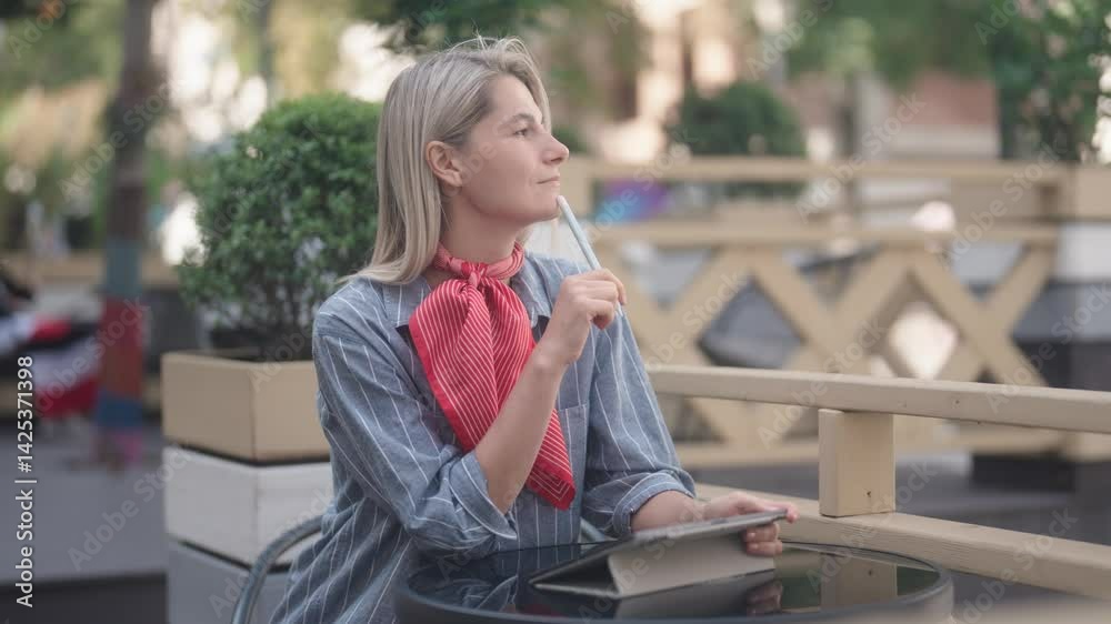 Woman sits and works on tablet outdoors using stylus pen. She takes a moment to contemplate her next move. A great scene for creative work or design projects. Woman sits and works on tablet outdoors using stylus pen. She takes a moment to contemplate her next move. A great scene for creative work or design projects.