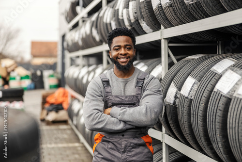 Obraz na płótnie Portrait of multicultural mechanic standing with arms crossed near tires. w salonie