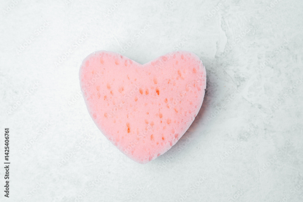 Fototapeta premium Cute heart-shaped sponge in light pink color on a textured surface