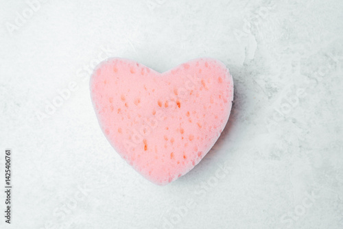 Cute heart-shaped sponge in light pink color on a textured surface