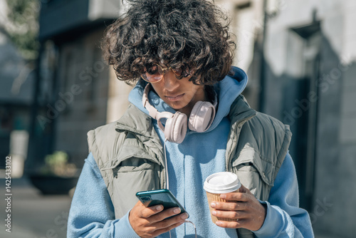 Teenage boy with headphones and mobile phone on the street eating a takeaway