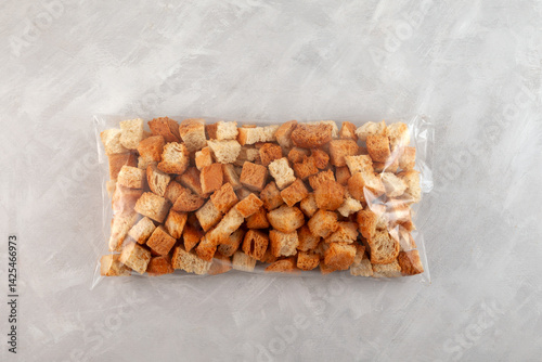 Photos Crunchy bread croutons in transparent plastic bag on grey background