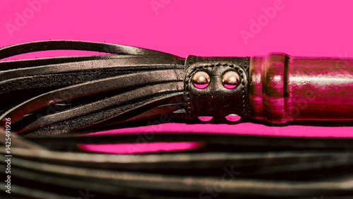 Photos bdsm attribute black leather lash on a red background close-up