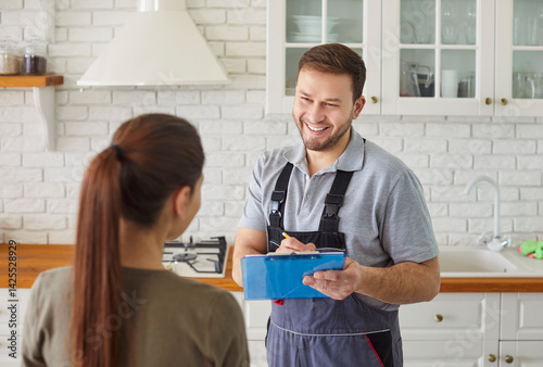 Man plumber talking with female client signing contract for plumbing services at home. Male mechanic or repairman consulting woman customer standing in kitchen. Maintenance and repair service.
